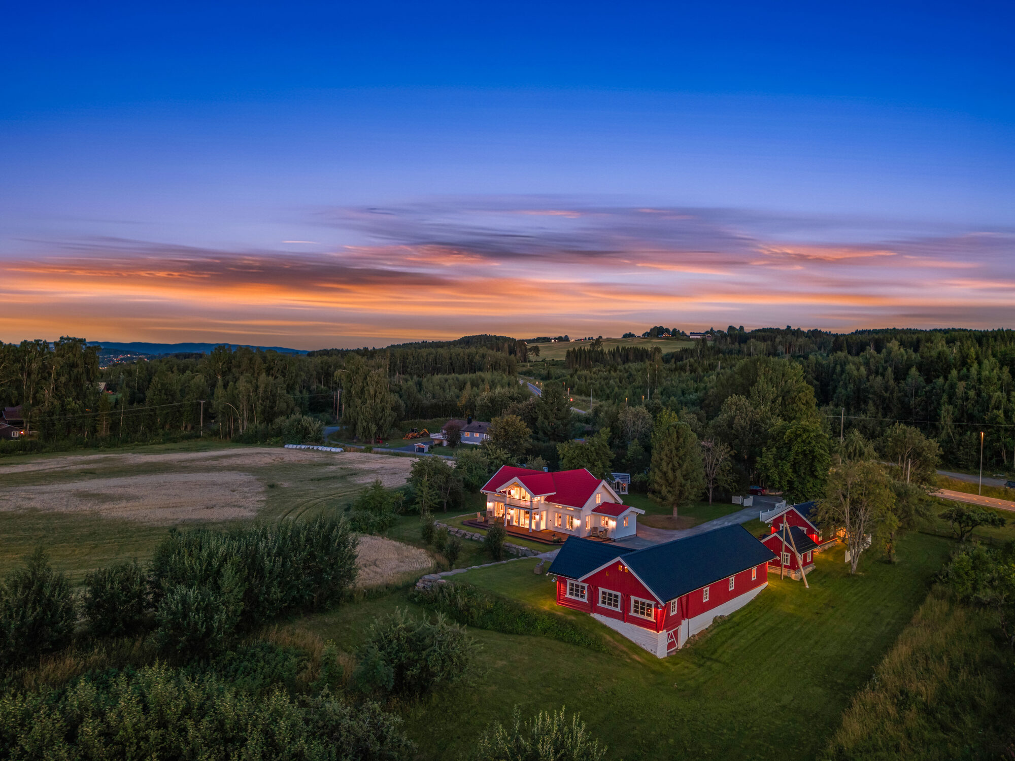 Luftfoto av gårdsbruk i kulturlandskap ved solnedgang